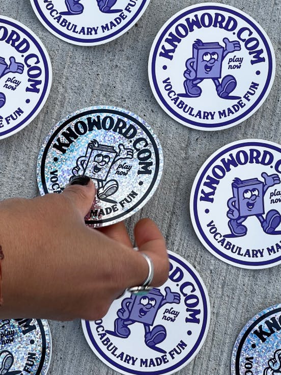 knoword stickers on the pavement, with a hand coming in from the left side of the frame to pick a glittery sticker up